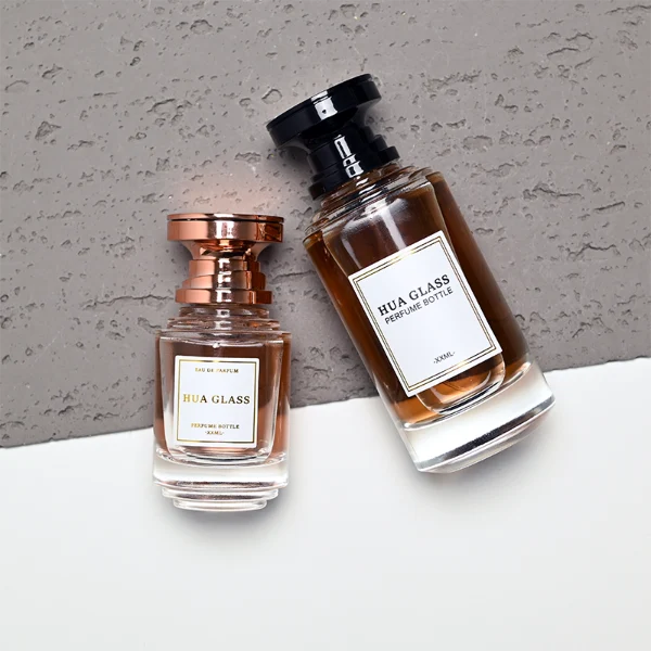 A thick-bottomed cylindrical glass perfume bottle featuring a round, curved profile with gradient color finish choices like black, blue, pink, or brown, topped with a uniquely styled injection-molded plastic cap in black or white.