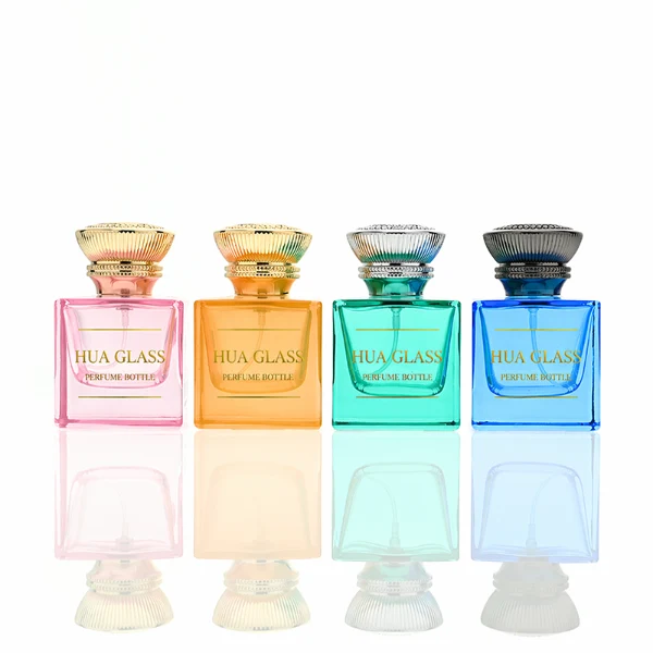 A thick-bottomed cube glass perfume bottle featuring an angular, square silhouette with semi-translucent or frosted colored finishes, topped with a heavy, uniquely ribbed metallic Zamac cap available in black, gold, or silver.