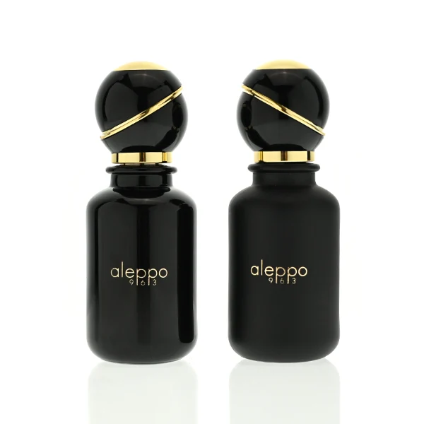  two cylindrical solid black perfume bottles stand side by side, one in a glossy finish and the other in a matte finish. Both bottles feature a gold logo that reads "aleppo 91613" and are topped with unique, spherical black caps encircled by a diagonal gold ribbon accent and a gold collar.