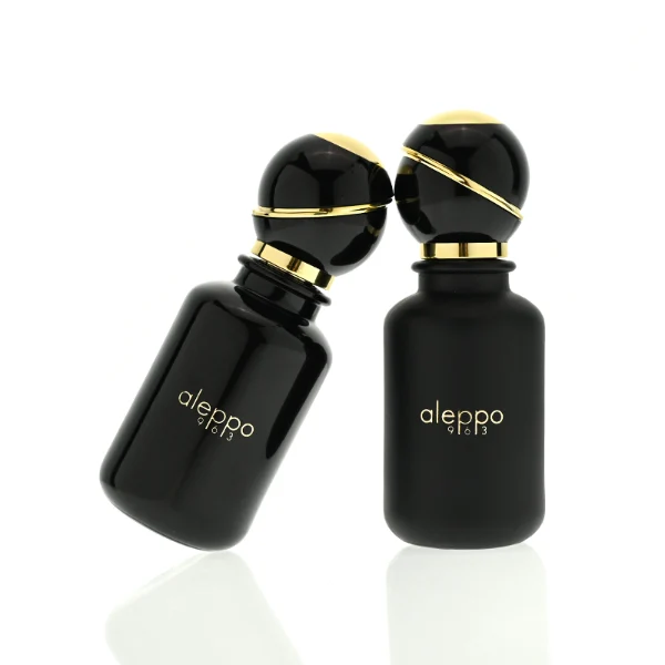 two cylindrical solid black perfume bottles stand side by side, one in a glossy finish and the other in a matte finish. Both bottles feature a gold logo that reads "aleppo 91613" and are topped with unique, spherical black caps encircled by a diagonal gold ribbon accent and a gold collar.