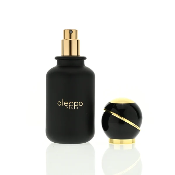 two cylindrical solid black perfume bottles stand side by side, one in a glossy finish and the other in a matte finish. Both bottles feature a gold logo that reads "aleppo 91613" and are topped with unique, spherical black caps encircled by a diagonal gold ribbon accent and a gold collar.