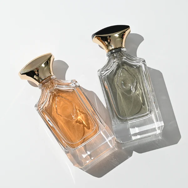 A diamond-cut rectangular clear glass perfume bottle with faceted corners and textured vertical ridges along the upper shoulders, paired with a unique flared, curved plastic cap available in solid gold or black-and-gold finish.