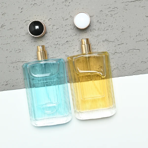 A rectangular clear glass perfume bottle detailed with distinct vertical grooves and a smooth central label indentation, paired with a cylindrical golden plastic cap featuring an intricate textured pattern.