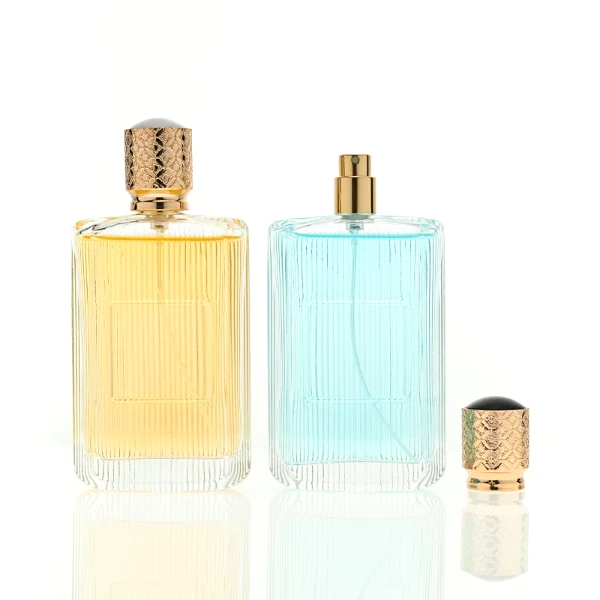 A rectangular clear glass perfume bottle detailed with distinct vertical grooves and a smooth central label indentation, paired with a cylindrical golden plastic cap featuring an intricate textured pattern.