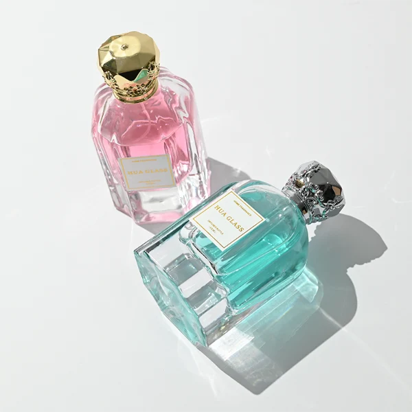 A hexagonal clear glass perfume bottle with structured vertical facets along the body, paired with an ornate, crown-shaped heavy metallic Zamac cap available in polished gold or silver.