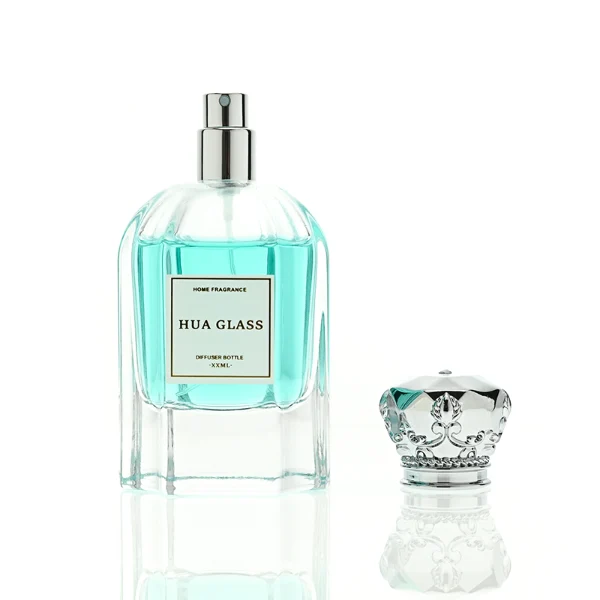 A hexagonal clear glass perfume bottle with structured vertical facets along the body, paired with an ornate, crown-shaped heavy metallic Zamac cap available in polished gold or silver.