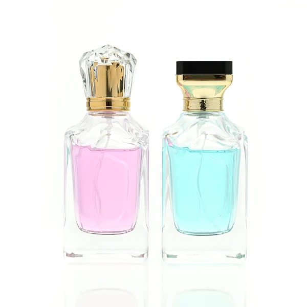 A thick-bottomed rectangular clear glass perfume bottle with faceted upper corners, shown with two cap variations: a crystal-clear faceted crown-shaped cap with a gold core, and a flared gold cap topped with a flat black cube block.