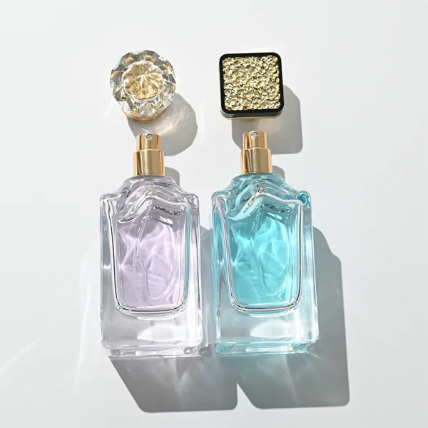 A thick-bottomed rectangular clear glass perfume bottle with faceted upper corners, shown with two cap variations: a crystal-clear faceted crown-shaped cap with a gold core, and a flared gold cap topped with a flat black cube block.