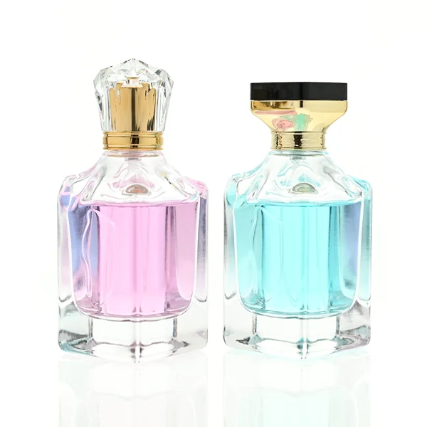 A thick-bottomed rectangular clear glass perfume bottle with faceted upper corners, shown with two cap variations: a crystal-clear faceted crown-shaped cap with a gold core, and a flared gold cap topped with a flat black cube block.