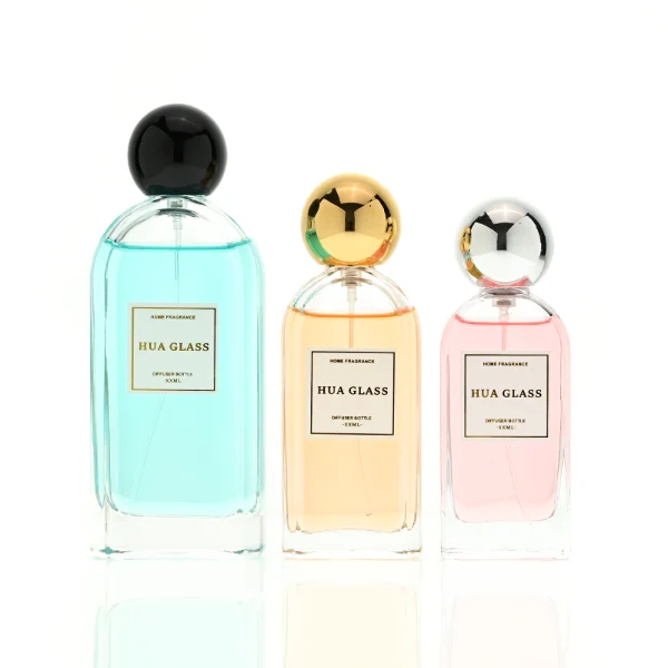 a set of rectangular clear glass perfume bottles features rounded shoulders and a thick glass base, each paired with a smooth, highly reflective spherical ball cap available in glossy black, metallic gold, or polished silver.