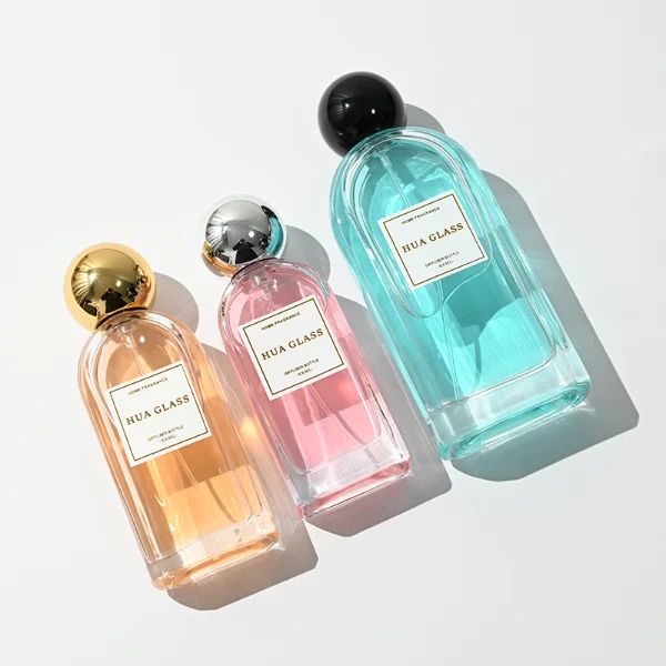 a set of rectangular clear glass perfume bottles features rounded shoulders and a thick glass base, each paired with a smooth, highly reflective spherical ball cap available in glossy black, metallic gold, or polished silver.