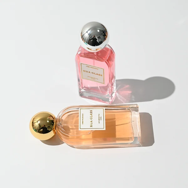 a set of rectangular clear glass perfume bottles features rounded shoulders and a thick glass base, each paired with a smooth, highly reflective spherical ball cap available in glossy black, metallic gold, or polished silver.