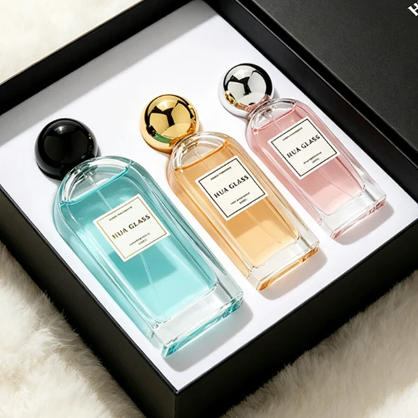 a set of rectangular clear glass perfume bottles features rounded shoulders and a thick glass base, each paired with a smooth, highly reflective spherical ball cap available in glossy black, metallic gold, or polished silver.