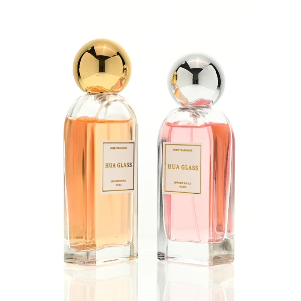 a set of rectangular clear glass perfume bottles features rounded shoulders and a thick glass base, each paired with a smooth, highly reflective spherical ball cap available in glossy black, metallic gold, or polished silver.
