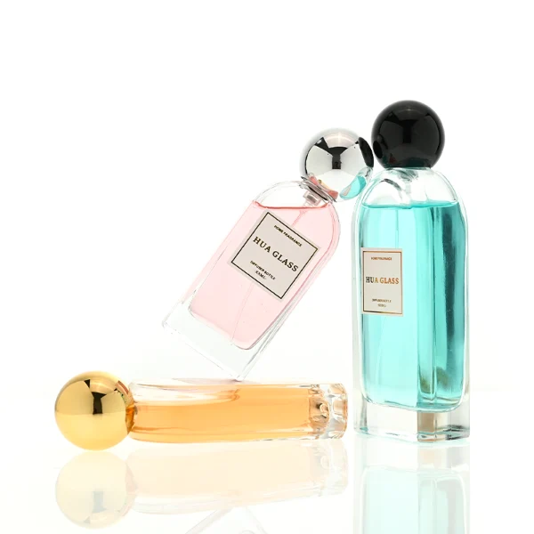 a set of rectangular clear glass perfume bottles features rounded shoulders and a thick glass base, each paired with a smooth, highly reflective spherical ball cap available in glossy black, metallic gold, or polished silver.