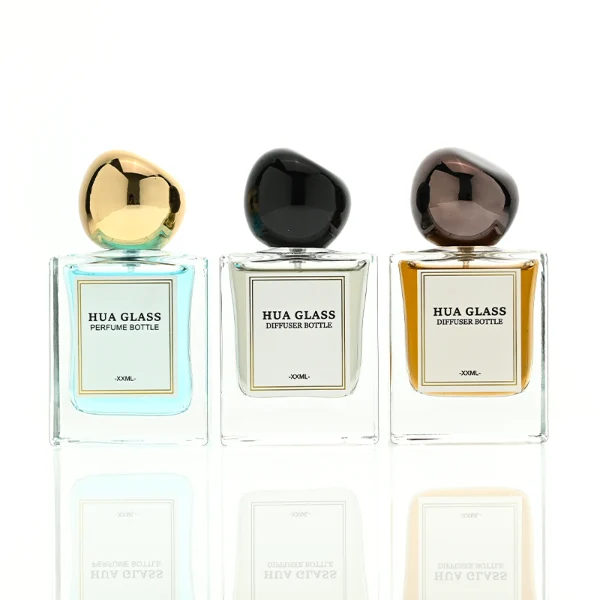 In the image, a thick-bottomed cube clear glass perfume bottle with a structured square silhouette is paired with a smooth, asymmetrical oval ellipse plastic cap available in polished gold, glossy black, or metallic brown finish.