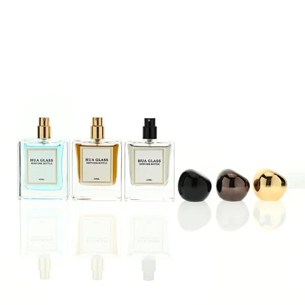 In the image, a thick-bottomed cube clear glass perfume bottle with a structured square silhouette is paired with a smooth, asymmetrical oval ellipse plastic cap available in polished gold, glossy black, or metallic brown finish.