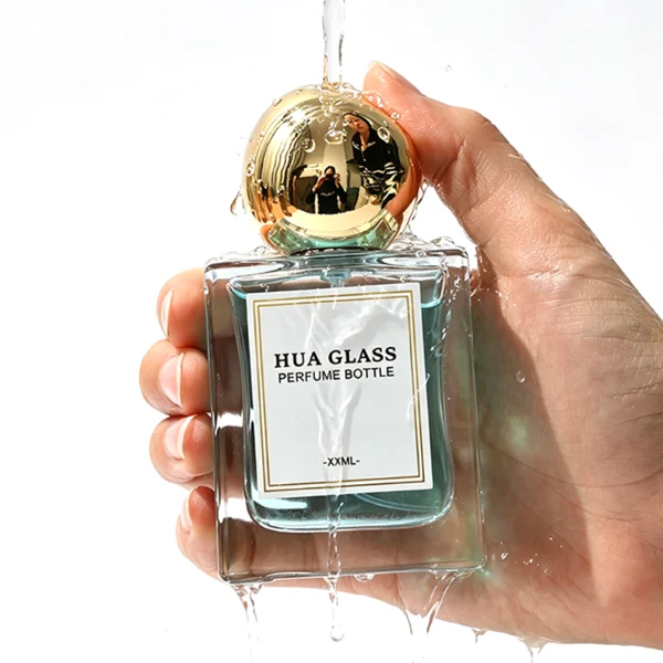 In the image, a thick-bottomed cube clear glass perfume bottle with a structured square silhouette is paired with a smooth, asymmetrical oval ellipse plastic cap available in polished gold, glossy black, or metallic brown finish.