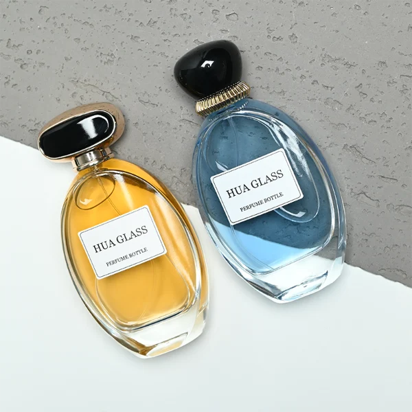 a globular curved clear glass perfume bottle features an oval silhouette with a heavy base, paired with a smooth, pebble-shaped plastic cap available in glossy solid black with a ribbed gold collar, or a flat-oval black design encased in a gold border.