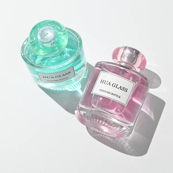 Based on the text description for image_128ca8.png, a clear square glass perfume bottle features rounded shoulders and a substantial, thick glass base, paired with a uniquely styled plastic cap available in pink-and-silver or blue-and-silver accents.