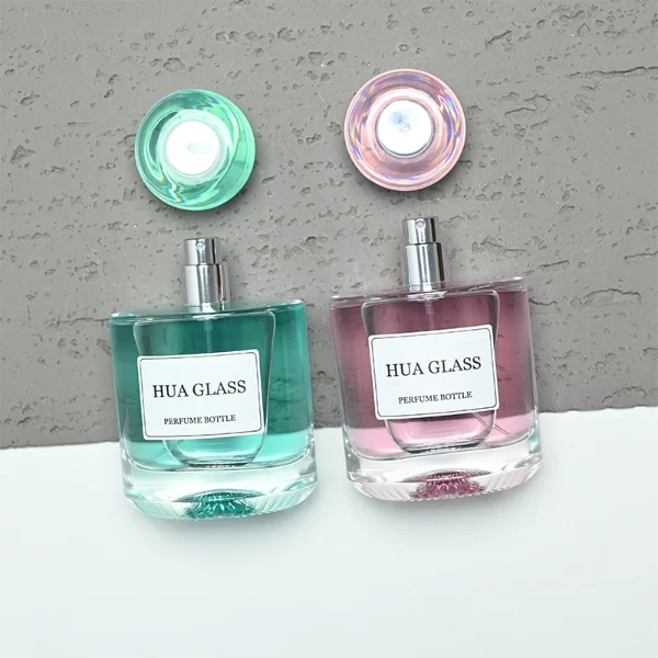 Based on the text description for image_128ca8.png, a clear square glass perfume bottle features rounded shoulders and a substantial, thick glass base, paired with a uniquely styled plastic cap available in pink-and-silver or blue-and-silver accents.