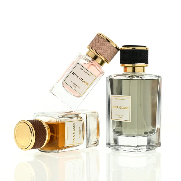 a clear rectangular glass perfume bottle features rounded shoulders and a thick square base, paired with a textured cylindrical plastic cap detailed with a micro-diamond knurled pattern and bordered by shiny gold metallic trim, available in black-and-gold or brown-and-gold finishes.