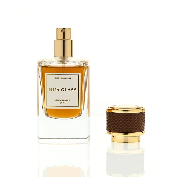 a clear rectangular glass perfume bottle features rounded shoulders and a thick square base, paired with a textured cylindrical plastic cap detailed with a micro-diamond knurled pattern and bordered by shiny gold metallic trim, available in black-and-gold or brown-and-gold finishes.