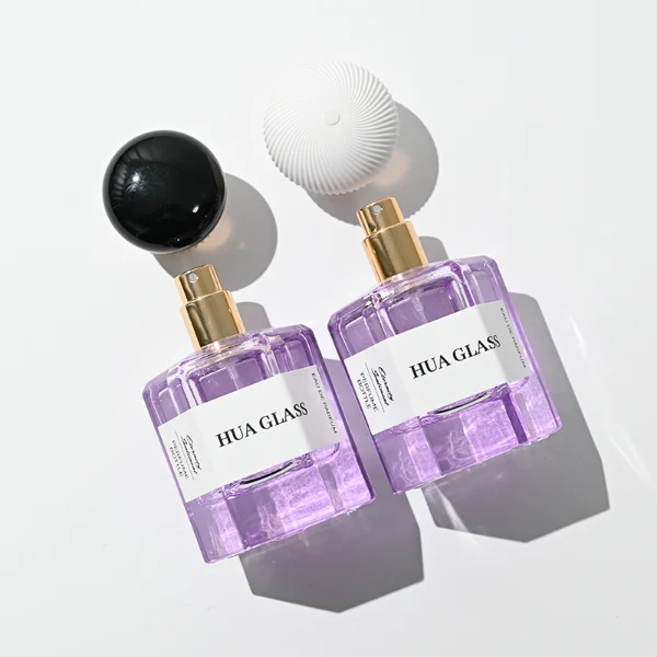 a hexagonal perfume bottle crafted from semi-translucent purple glass features a structured angular silhouette, paired with a pebble cobblestone-shaped plastic cap. The cap is available as either a smooth glossy black or a textured, vertically-ribbed matte white dome, both sitting atop an elegant, braided metallic gold collar.