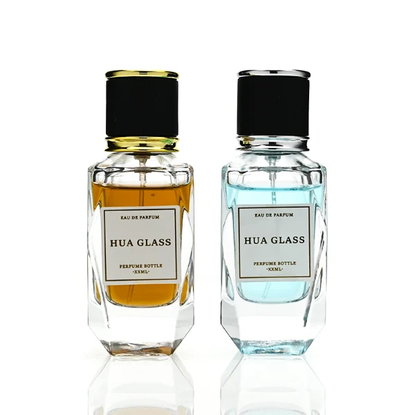 a classic rectangular clear glass perfume bottle with a heavy, thick base and faceted edges is paired with a matte black cylindrical cap. The cap is bordered at the top and bottom by a polished metallic ring, available in a bright gold or silver finish.