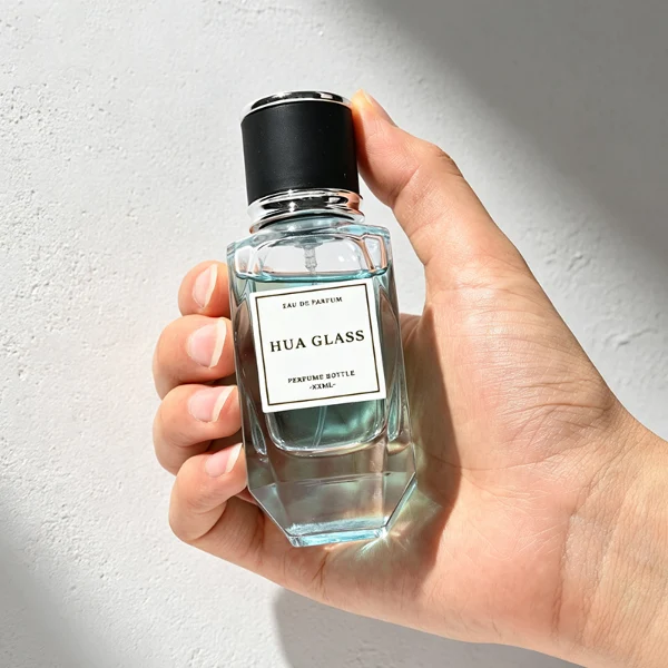 a classic rectangular clear glass perfume bottle with a heavy, thick base and faceted edges is paired with a matte black cylindrical cap. The cap is bordered at the top and bottom by a polished metallic ring, available in a bright gold or silver finish.
