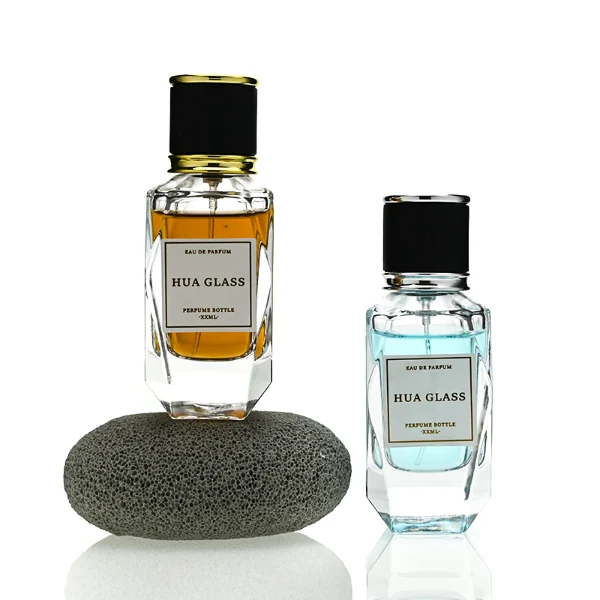 a classic rectangular clear glass perfume bottle with a heavy, thick base and faceted edges is paired with a matte black cylindrical cap. The cap is bordered at the top and bottom by a polished metallic ring, available in a bright gold or silver finish.