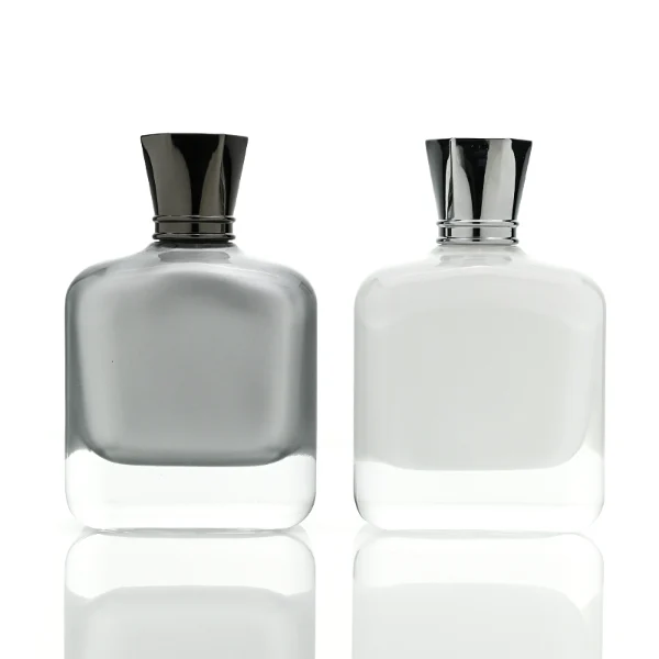 Two smooth rectangular glass perfume bottles with rounded corners and thick clear bases. One features an inner-sprayed metallic silver finish with a gunmetal black multifaceted geometric cap, while the other features an inner-sprayed opaque white finish topped with a chrome silver geometric cap.