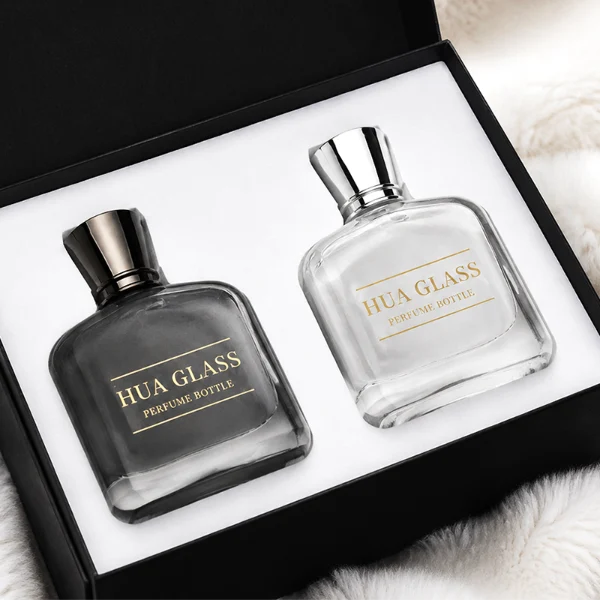 Two smooth rectangular glass perfume bottles with rounded corners and thick clear bases. One features an inner-sprayed metallic silver finish with a gunmetal black multifaceted geometric cap, while the other features an inner-sprayed opaque white finish topped with a chrome silver geometric cap.