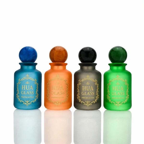 A lineup of four cylindrical frosted glass perfume bottles in matte shades of blue, orange, dark grey, and green. Each bottle is paired with a matching large spherical ball cap featuring a glossy, marbled stone texture in deep blue, amber brown, black, and forest green.