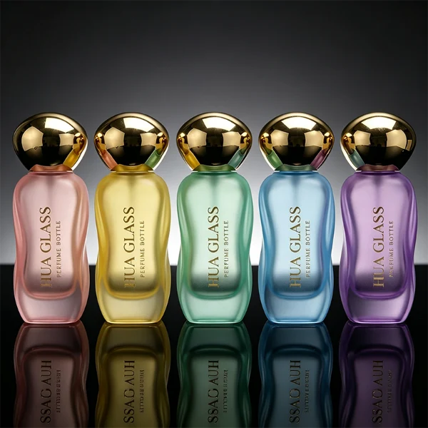 Three clear glass perfume bottles featuring smoothly curved organic shapes and heavy transparent bases, filled with olive green, pale pink, and light green liquids. The bottles are topped with smooth, pebble-like bulbous round caps, displayed in glossy black, polished metallic gold, and high-shine metallic silver finishes.