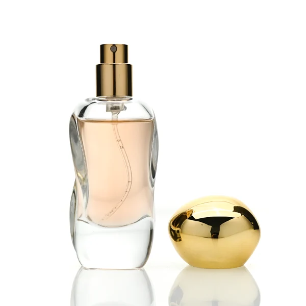 Three clear glass perfume bottles featuring smoothly curved organic shapes and heavy transparent bases, filled with olive green, pale pink, and light green liquids. The bottles are topped with smooth, pebble-like bulbous round caps, displayed in glossy black, polished metallic gold, and high-shine metallic silver finishes.