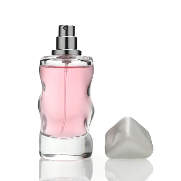 A lineup of four clear glass perfume bottles featuring unique, wave-curved organic sides and heavy transparent bases. The bottles are filled with yellow, pink, light blue, and amber liquids, each topped with an asymmetrical, abstract artistic cap resembling a tumbled stone or distorted cube in glossy mustard yellow, light grey, periwinkle blue, and solid black finishes.