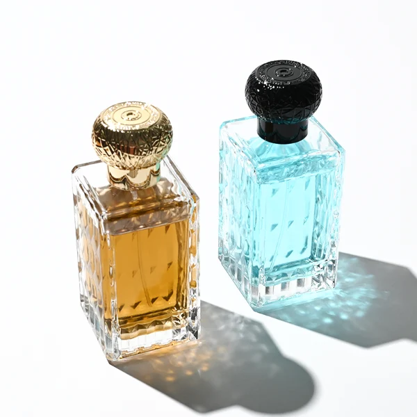 three clear rectangular glass perfume bottles feature deeply textured, diamond-faceted faces and geometric patterned side walls, holding bright blue, pale pink, and deep amber liquids. Each bottle is topped with an ornate, spherical textured ball cap featuring a heavily cracked or webbed aesthetic, shown in matte black, polished silver, and bright gold finishes.