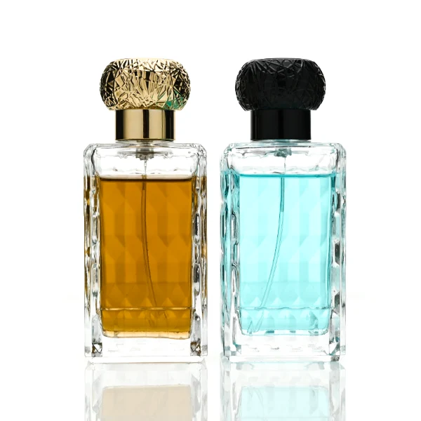 three clear rectangular glass perfume bottles feature deeply textured, diamond-faceted faces and geometric patterned side walls, holding bright blue, pale pink, and deep amber liquids. Each bottle is topped with an ornate, spherical textured ball cap featuring a heavily cracked or webbed aesthetic, shown in matte black, polished silver, and bright gold finishes.