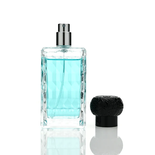 three clear rectangular glass perfume bottles feature deeply textured, diamond-faceted faces and geometric patterned side walls, holding bright blue, pale pink, and deep amber liquids. Each bottle is topped with an ornate, spherical textured ball cap featuring a heavily cracked or webbed aesthetic, shown in matte black, polished silver, and bright gold finishes.