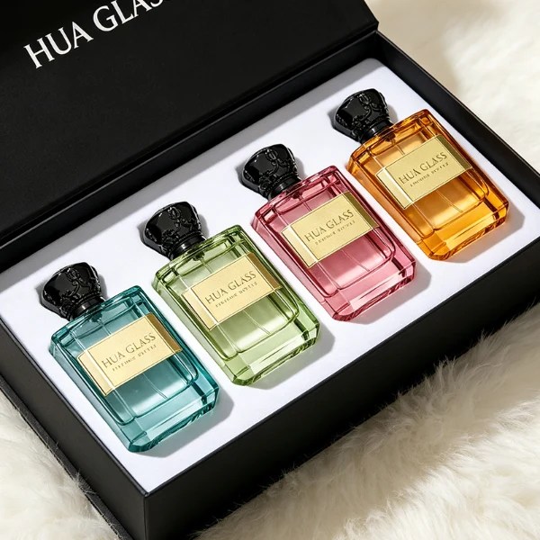 Two flat rectangular clear glass perfume bottles are shown with faceted, angled bottom corners and thick glass bases, holding light blue and amber liquids. Each bottle features a subtle debossed rectangular label panel on the front and is topped with an ornate, heavy Zamac crown-motif cap with a faceted dome, finished in glossy black and polished gold.