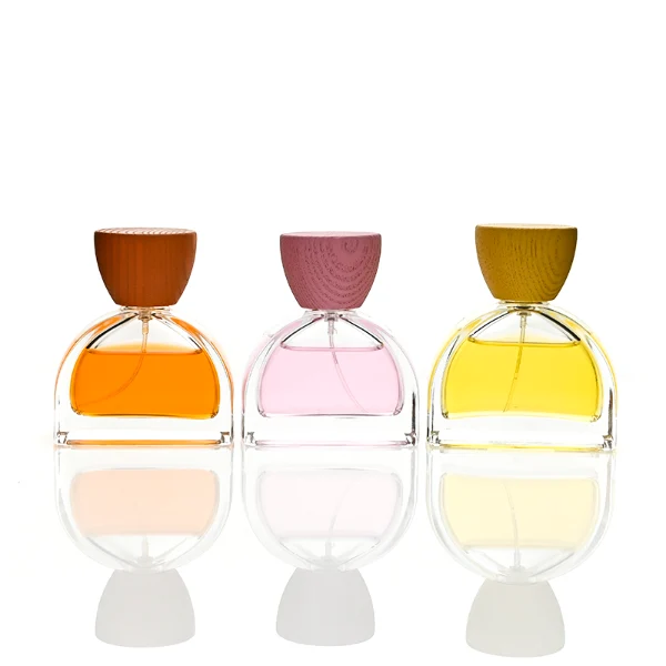three clear glass perfume bottles feature a distinctive semi-circular arch silhouette with a flat base, holding vibrant orange, soft pink, and bright yellow liquids. Each bottle is topped with an upward-flaring, wide-mouth natural solid wood cap displaying prominent wood-grain textures, finished in stained shades of terracotta orange, dusty rose pink, and mustard yellow.