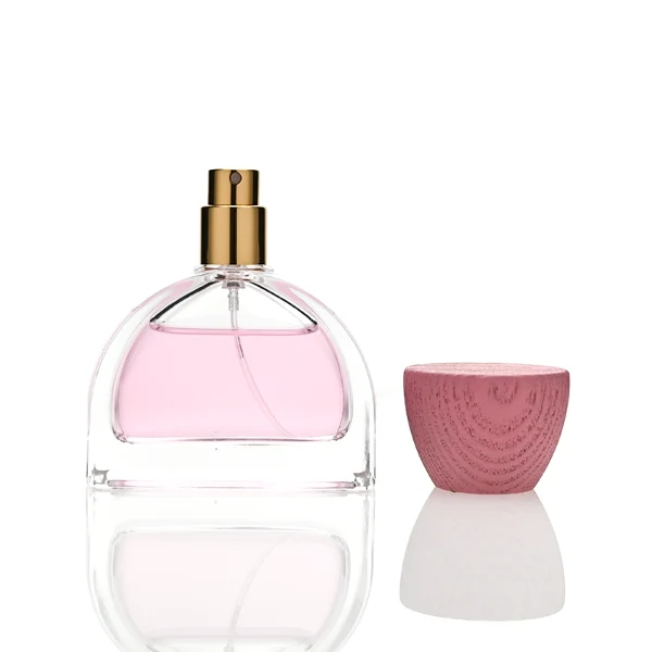 three clear glass perfume bottles feature a distinctive semi-circular arch silhouette with a flat base, holding vibrant orange, soft pink, and bright yellow liquids. Each bottle is topped with an upward-flaring, wide-mouth natural solid wood cap displaying prominent wood-grain textures, finished in stained shades of terracotta orange, dusty rose pink, and mustard yellow.