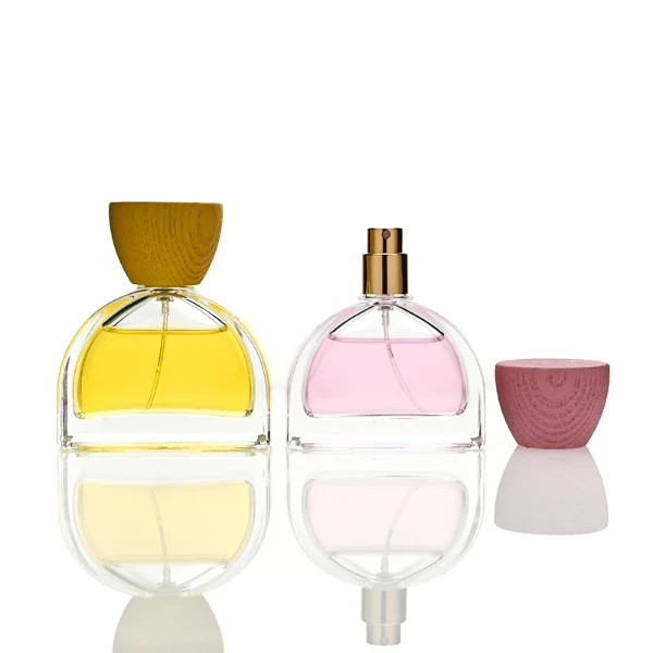 three clear glass perfume bottles feature a distinctive semi-circular arch silhouette with a flat base, holding vibrant orange, soft pink, and bright yellow liquids. Each bottle is topped with an upward-flaring, wide-mouth natural solid wood cap displaying prominent wood-grain textures, finished in stained shades of terracotta orange, dusty rose pink, and mustard yellow.