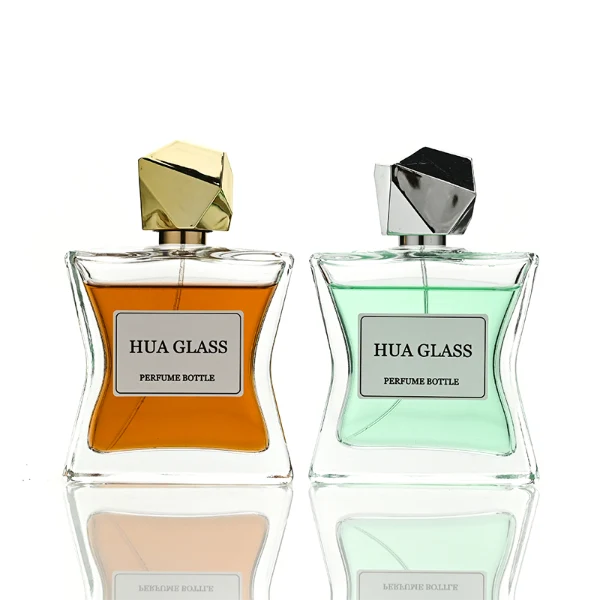 Two clear rectangular glass perfume bottles with a distinctively sculpted waisted design holding amber and light green liquids are shown. Each bottle features a central square white label and is topped with an asymmetrical, irregular multifaceted geometric cap featuring sharp reflective angles, presented in polished gold and high-shine chrome silver finishes.