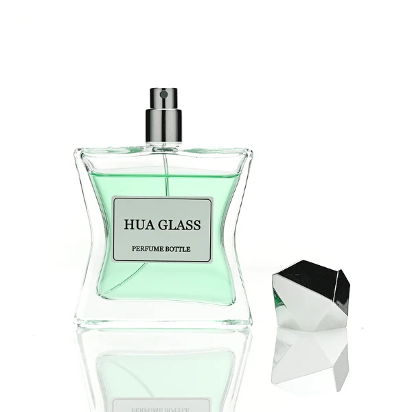 Two clear rectangular glass perfume bottles with a distinctively sculpted waisted design holding amber and light green liquids are shown. Each bottle features a central square white label and is topped with an asymmetrical, irregular multifaceted geometric cap featuring sharp reflective angles, presented in polished gold and high-shine chrome silver finishes.