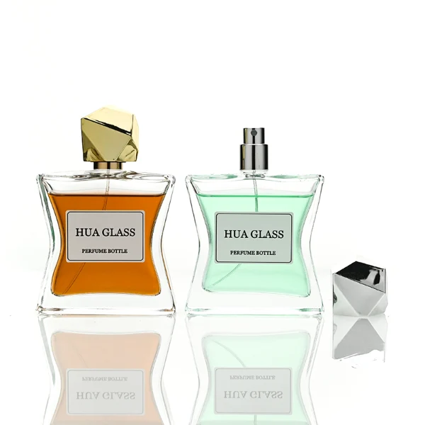 Two clear rectangular glass perfume bottles with a distinctively sculpted waisted design holding amber and light green liquids are shown. Each bottle features a central square white label and is topped with an asymmetrical, irregular multifaceted geometric cap featuring sharp reflective angles, presented in polished gold and high-shine chrome silver finishes.