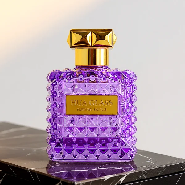 Two square semi-translucent violet glass perfume bottles are shown in 50ml and 100ml sizes, featuring an all-over rockstud-inspired studded diamond texture surrounding a smooth rectangular center panel. Each bottle is topped with a heavy, premium polished golden Zamac square geometric cap with a short cylindrical collar.