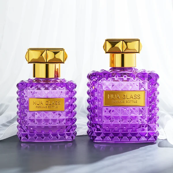 Two square semi-translucent violet glass perfume bottles are shown in 50ml and 100ml sizes, featuring an all-over rockstud-inspired studded diamond texture surrounding a smooth rectangular center panel. Each bottle is topped with a heavy, premium polished golden Zamac square geometric cap with a short cylindrical collar.