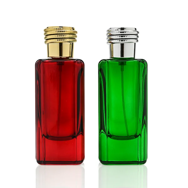 two tall rectangular, thick-bottomed glass perfume bottles are shown standing side by side. One bottle is made of vivid semi-translucent red glass and the other is vibrant semi-translucent green glass. Each bottle features subtly debossed vertical panels along its sides and is topped with a cylindrical cap encircled by a textured, coiling snake pattern—presented in polished gold on the red bottle and polished silver on the green bottle.